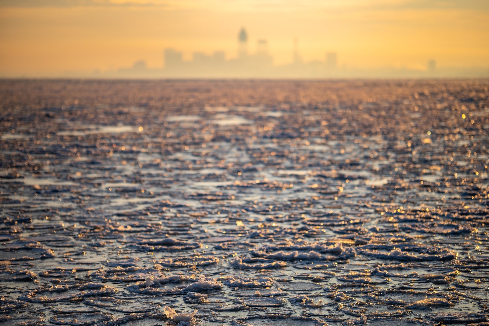 Broken ice on Lake Erie at sunrise, with the downtown Cleveland skyline hazy on the horizon